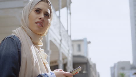 animación de una mujer asiática en hijab sentada y usando un teléfono inteligente sobre el paisaje urbano