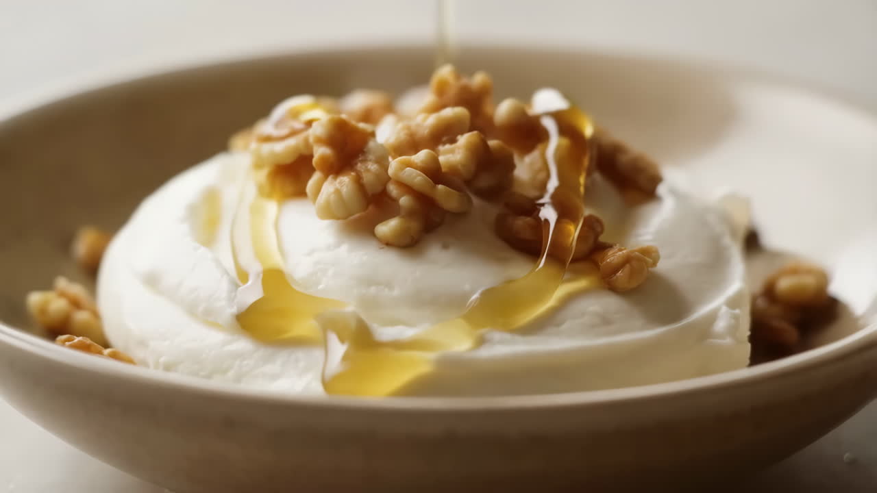 Closeup Bowl Of Yogurt With Walnuts, Golden Honey Pouring Into Whipped Creamy Surface, Glossy Drizzle