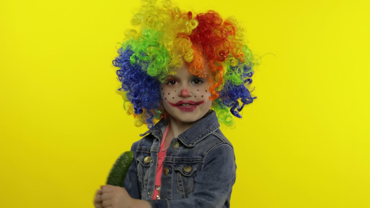 una pequeña niña payasa con una peluca colorida haciendo caras tontas, cantando, sonriendo, bailando. halloween