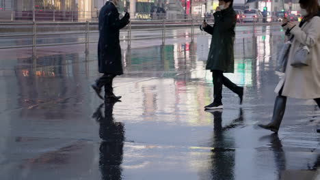 fashionable people in mask walking on wet road holding umbrella during snowfall evening in tokyo, japan