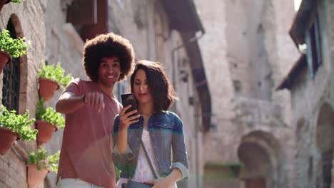 tourists using smartphone to search amenities or landmarks in rural town.slow motion. two people smiling while using smartphone outdoor in rural town.portrait medium shot.friends trip in italy