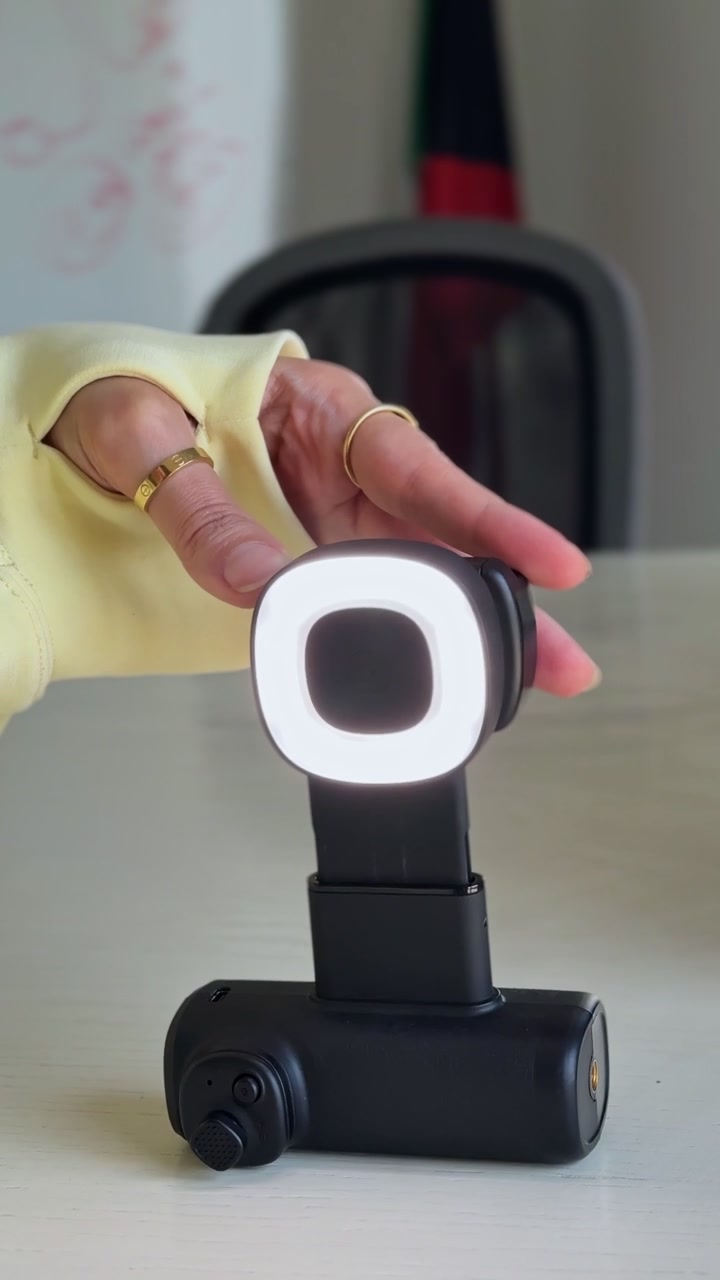 Primo piano di una mano che regola una luce di riempimento LED compatta su un rig per riprese con smartphone appoggiato su una scrivania, preparato per la creazione di contenuti verticali al chiuso