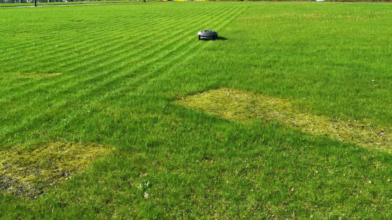 obotic lawnmower moving across large green field with striped grass