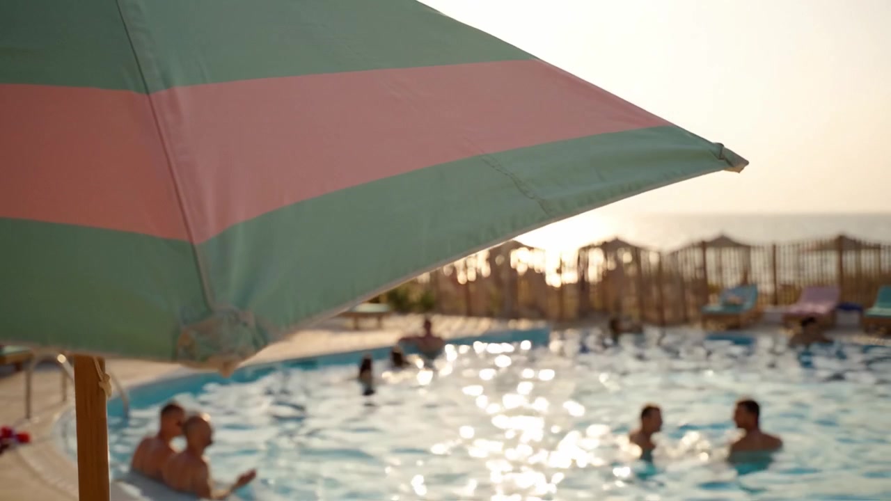 Tramonto tranquillo in una piscina a bordo spiaggia, che evidenzia sabbia, ombrellone e un'atmosfera rilassante con persone che si godono una serata serena in riva all'acqua