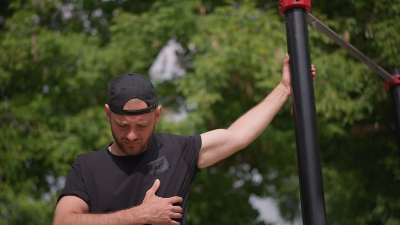 Person Checks Breathing After Exercise, Casual Man Observes Posture Following Outdoor Fitness Routine, Relaxed Individual Surveys Their Stance After Outdoor Calisthenics In Sunny Park Environment