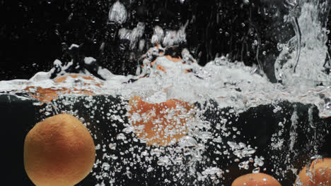 video of oranges falling into water with copy space on black background