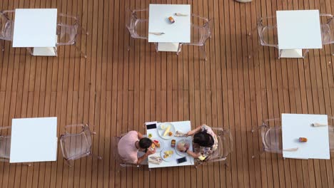 Couple-on-vacation-enjoy-summer-morning-eating-and-drinking-outdoor-breakfast-at-hotel-restaurant-with-waitress-serving-at-table