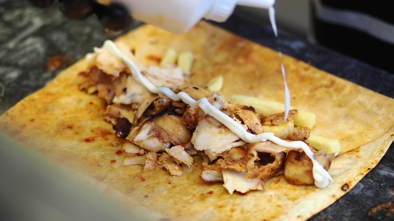 Chef che aggiunge salsa a un involtino di shawarma di pollo