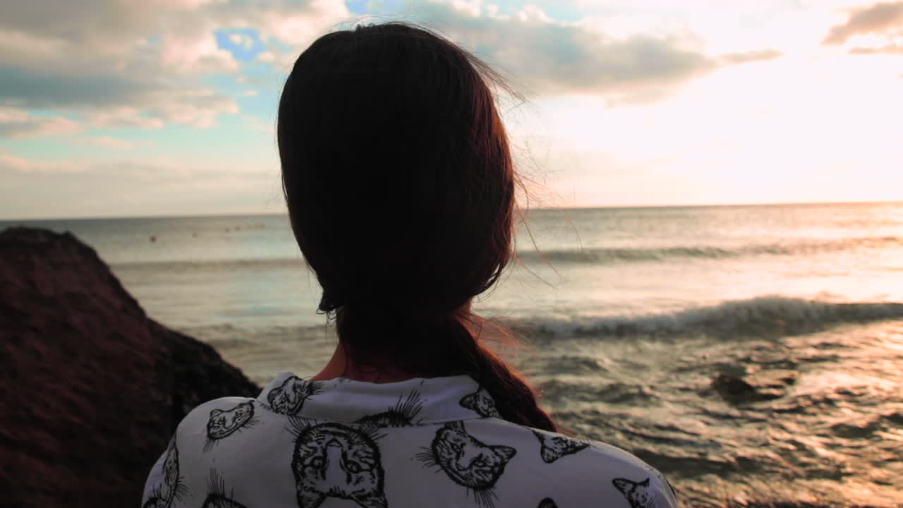 Brunette looking at the sunset on the ocean, moody close shot.