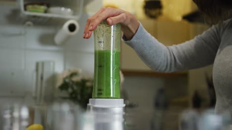 Caucasian-woman-preparing-green-vegetable-smoothie-in-kitchen