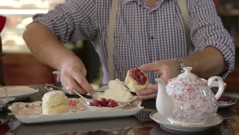 ein mann, der tee und scones mit marmelade und sahne trinkt