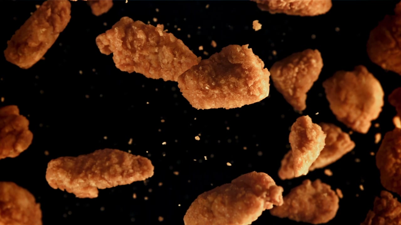 Nuggets de pollo fritos cayendo en cámara lenta sobre fondo negro