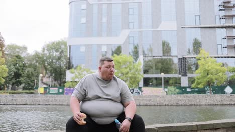 a fat man eats a hamburger and drinks water while exercising in the park the problem of overweight a fat man eats a hamburger and drinks water while exercising in the park the problem of overweight in a young person