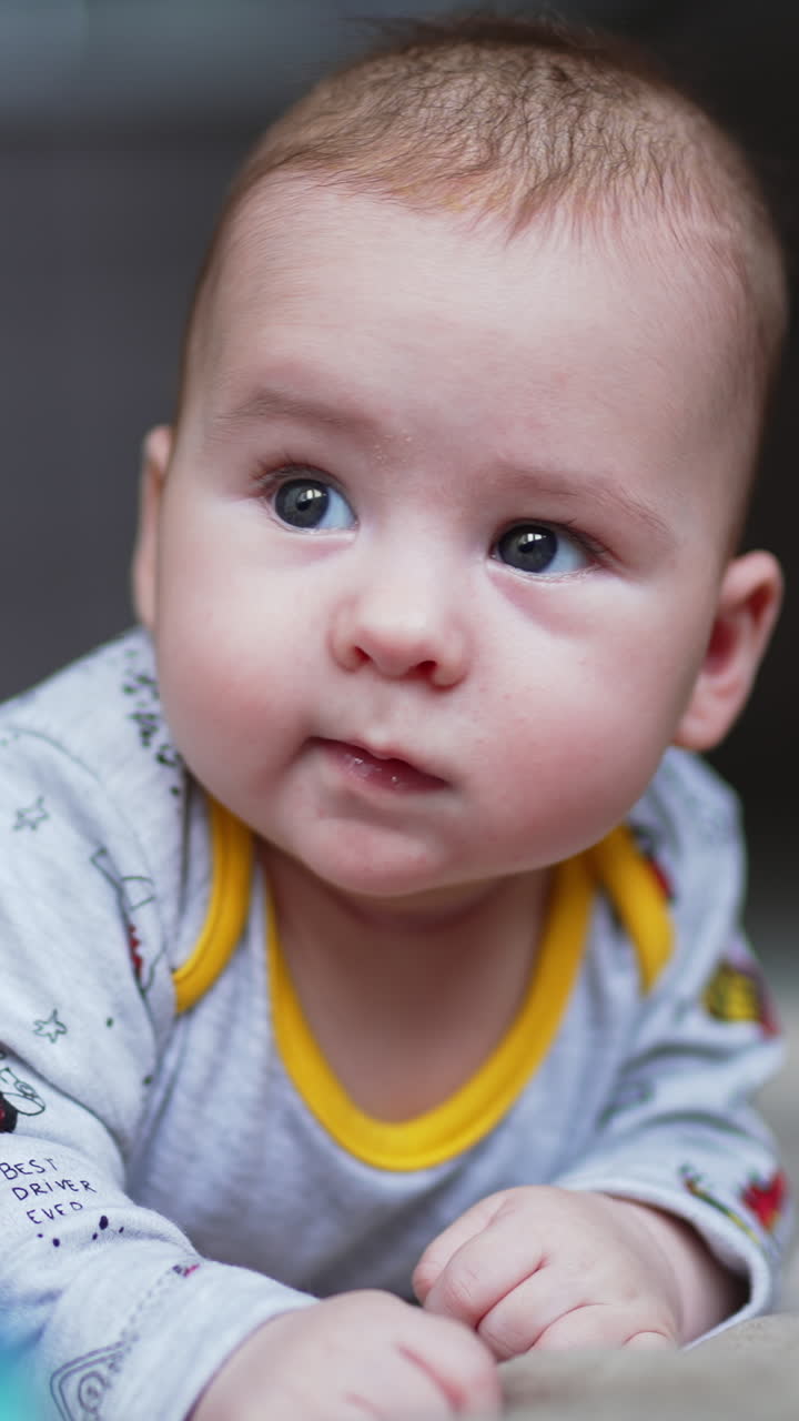 Cute adorable baby boy lies on tummy looking aside. Lovely beautiful kid smiling sweetly to something. Close up. Vertical video
