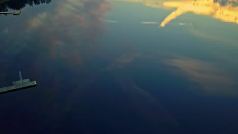 el cielo y las montañas se reflejan en la superficie de un lago y luego giran para revelar muelles de madera a lo largo de la costa de un pueblo - antena