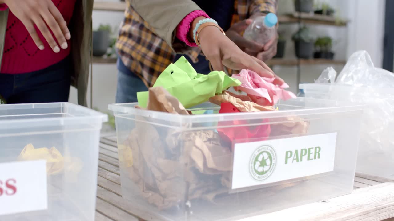 sección media de una pareja afroamericana recogiendo reciclaje en casa, en cámara lenta