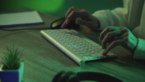 Male-hands-typing-on-the-keyboard-working-with-a-computer-on-a-neon-light-colorful-background.-Close-up.