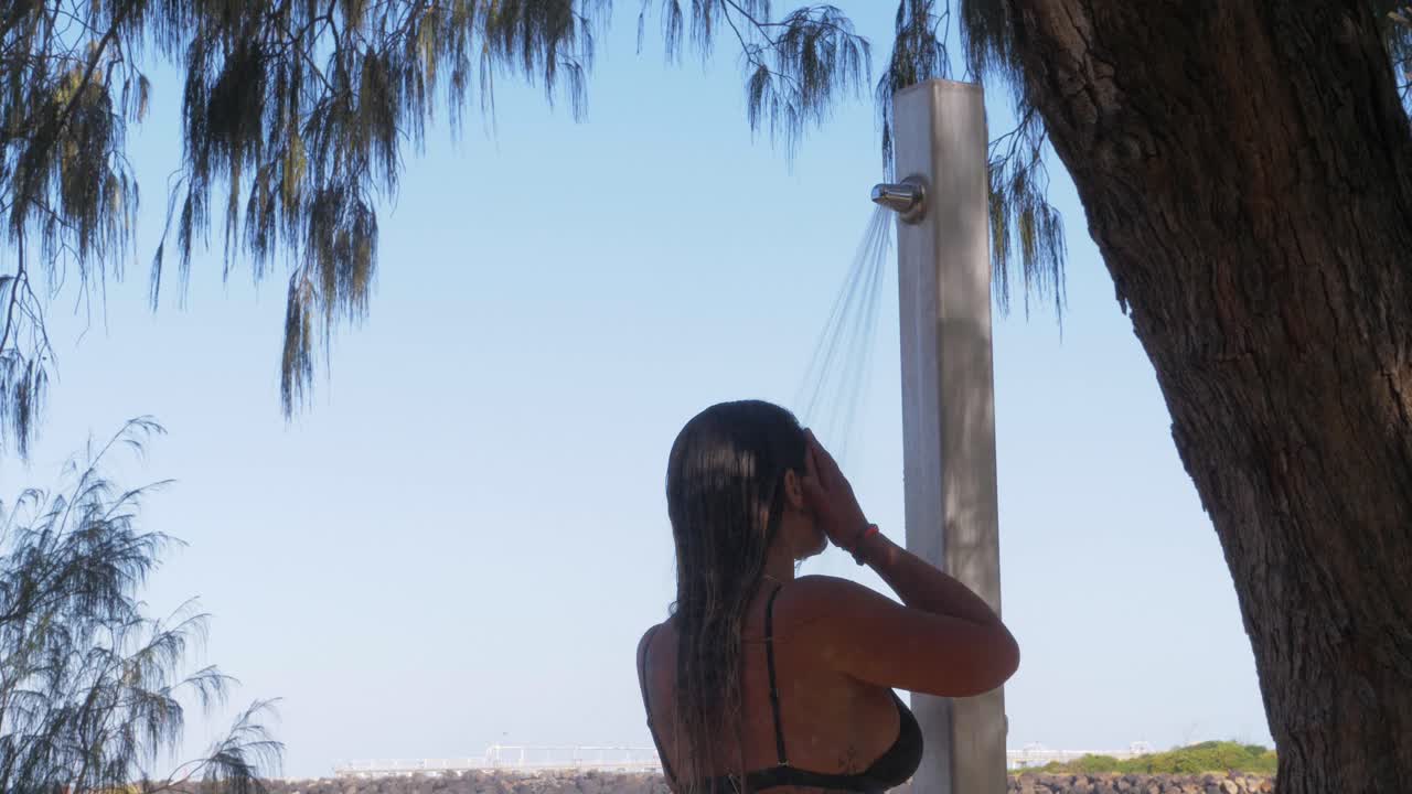 mujer duchándose bajo el árbol en la playa después de nadar en el océano - playa de duranbah en verano - nueva gales del sur, australia