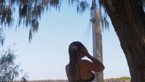 Woman-Taking-A-Shower-Under-The-Tree-On-The-Beach-After-Swimming-In-The-Ocean---Duranbah-Beach-In-Summer---New-South-Wales,-Australia