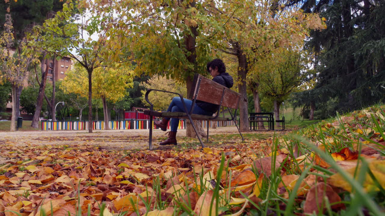Donna seduta su una panchina del parco in autunno con foglie cadute