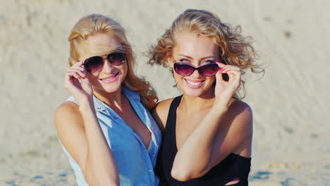 two young women posing for the camera smiling on the beach on a sunny day