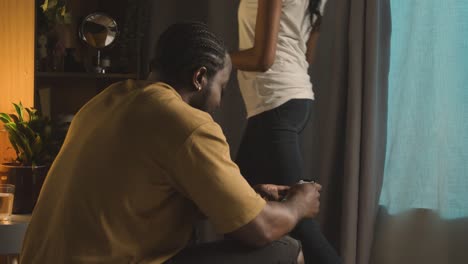 Young-Couple-Relaxing-At-Home-At-Night-With-Man-Scrolling-Internet-On-Mobile-Phone