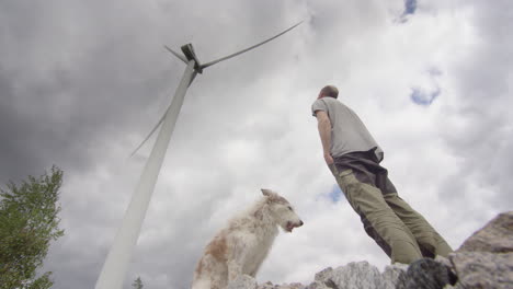 one man and his dog stand below a huge wind turbine, before walking away