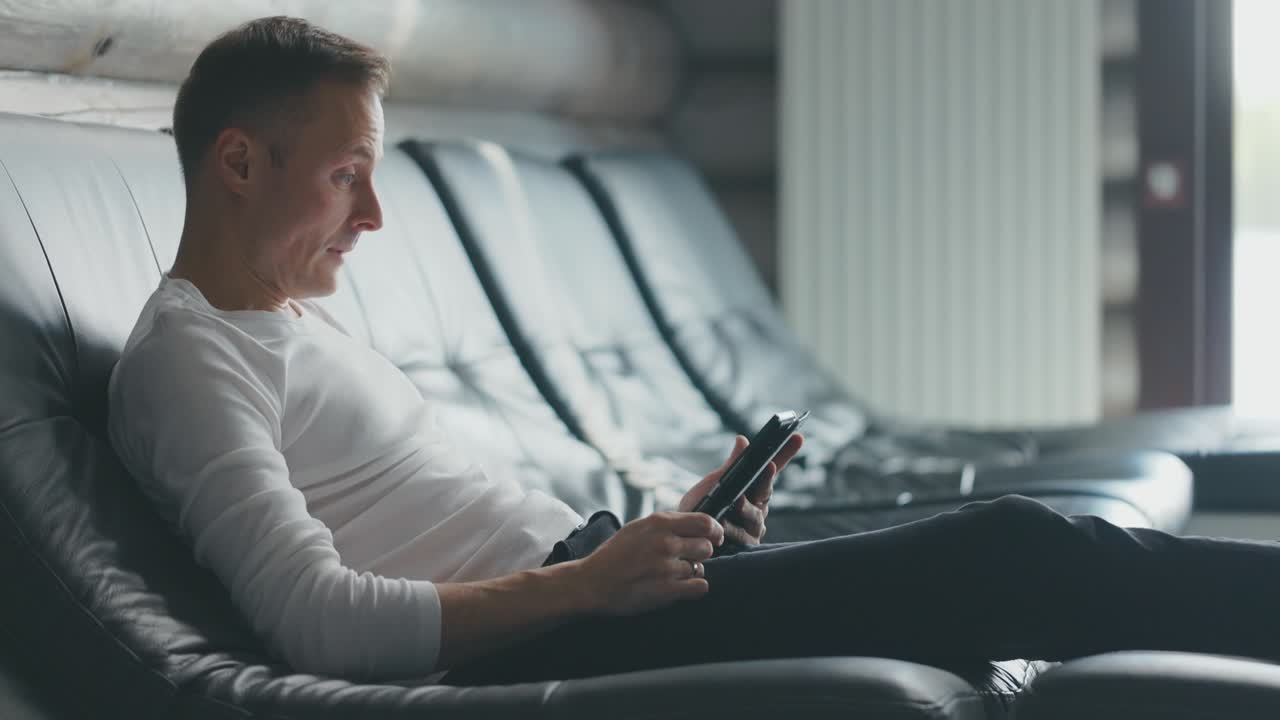 Man sits on sofa, uses tablet and rejoices at the received good news. Happy man reading good news on tablet