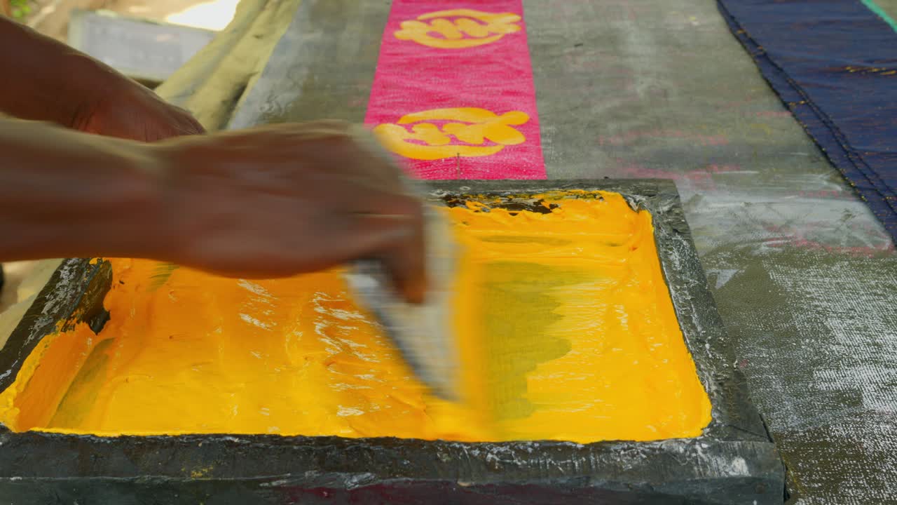 Tampilan dekat pekerja Afrika mencetak simbol yang dilukis pada tekstil Kente