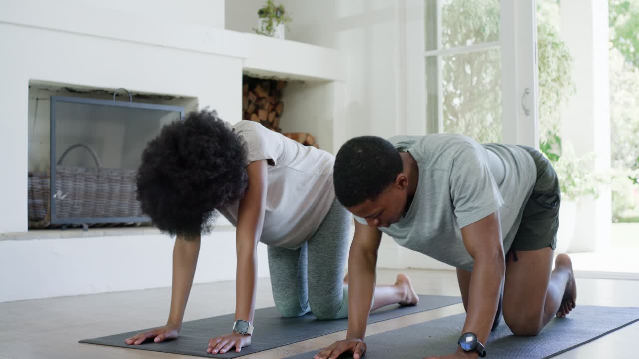 Couple starting bird-dog routine at home, extending arm and leg on black mats to build core