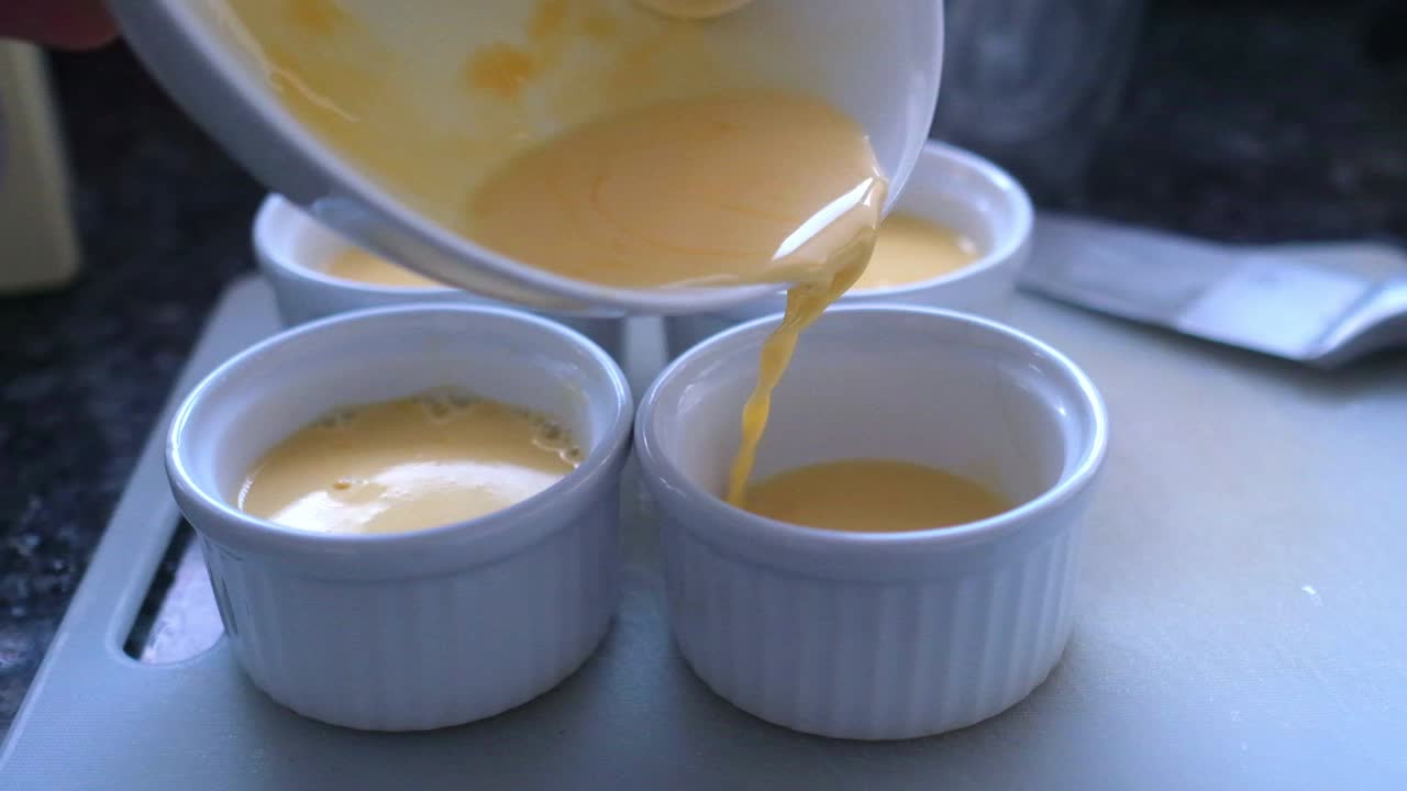 Membuat hidangan penutup Prancis crème brûlée, menuangkan adonan ke dalam mangkuk kecil dalam gerakan lambat
