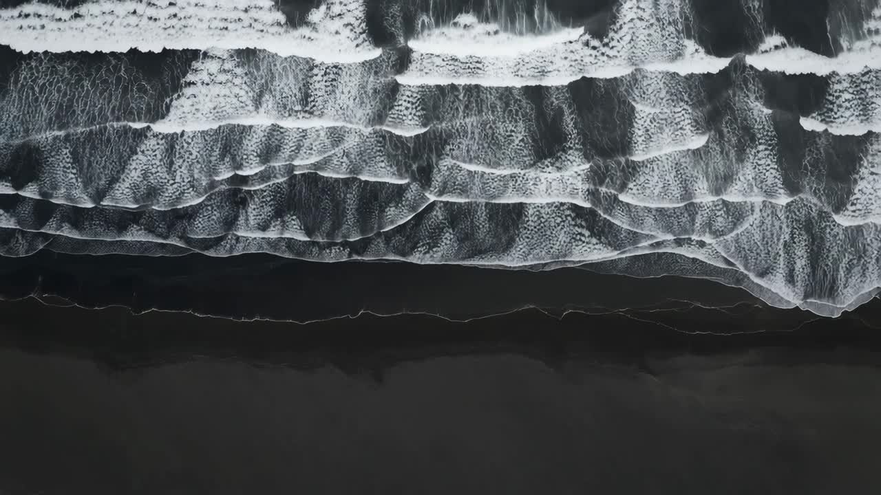 Aerial view of ocean waves crashing on a dark beach, captured from above