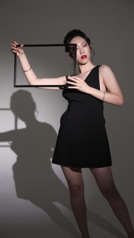 vertical video: asian woman in black dress posing with frame, creating artistic shadow effect
