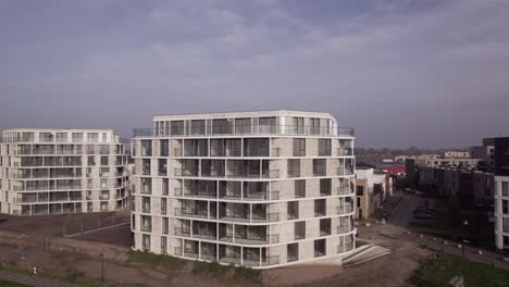 aerial sideways reveal of rising exterior facades of newly build luxury apartment towers pracht along riverside of river ijssel seen from above.
