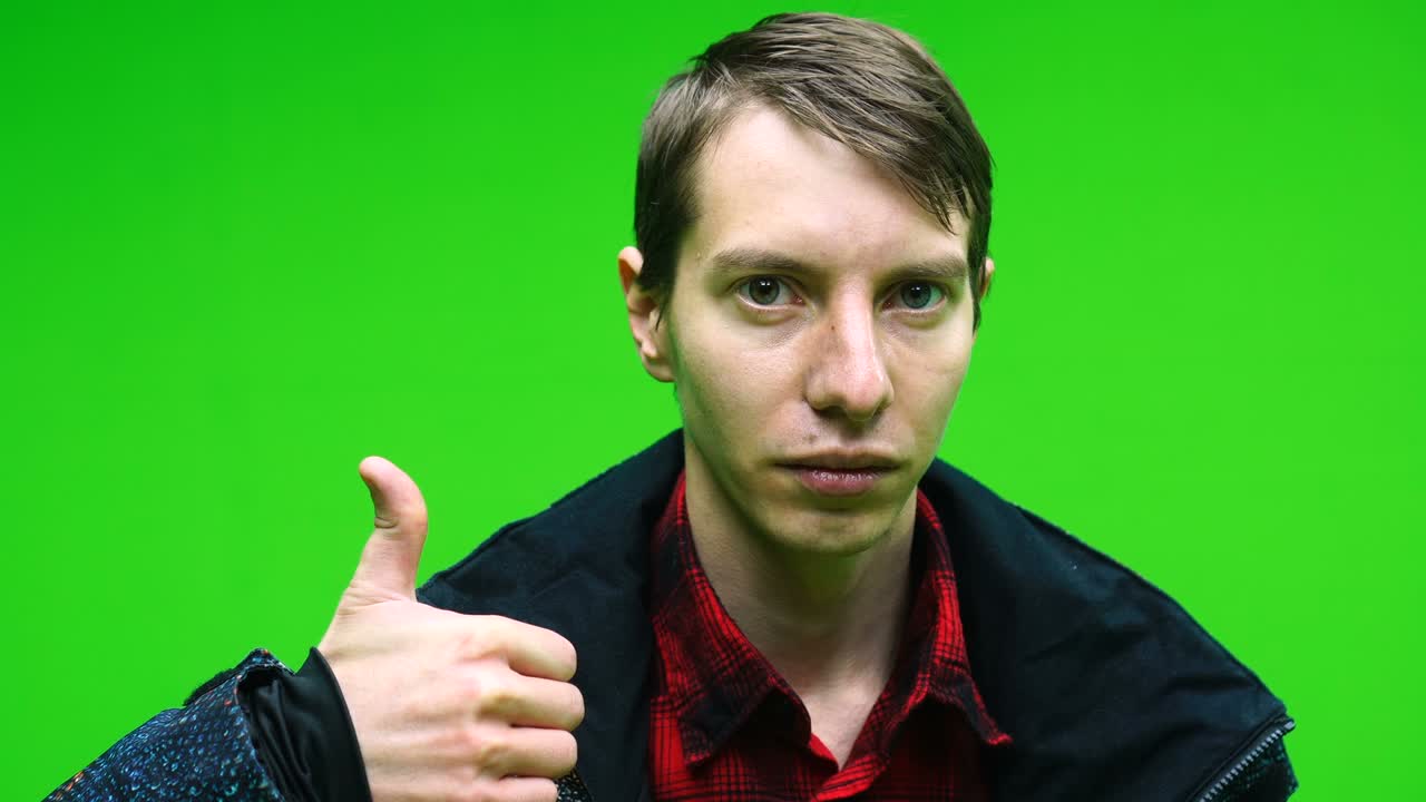 녹색 화면 배경에 엄지손가락을 보여주는 캐주얼 옷을 입은 긍정적인 젊은 남자.