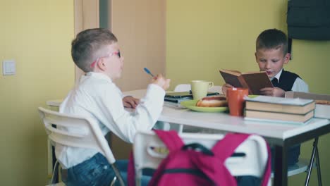 boy play with pen schoolmate reads book at table in canteen