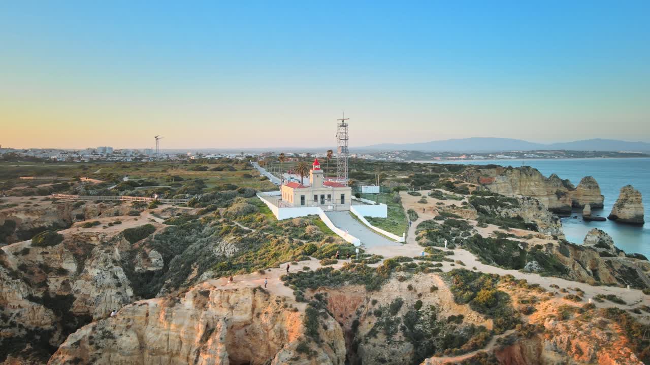 Camera spirals around Ponta da Piedade lighthouse, capturing rugged cliffs, coastal trails, and sweeping Atlantic views under the clear Algarve sky