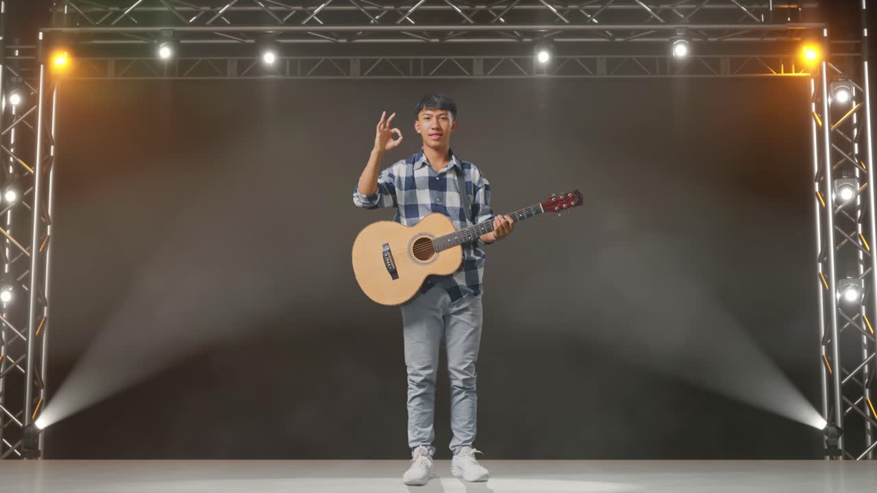 cuerpo lleno de adolescente asiático con guitarra mostrando bien gesto y sonriendo en el escenario