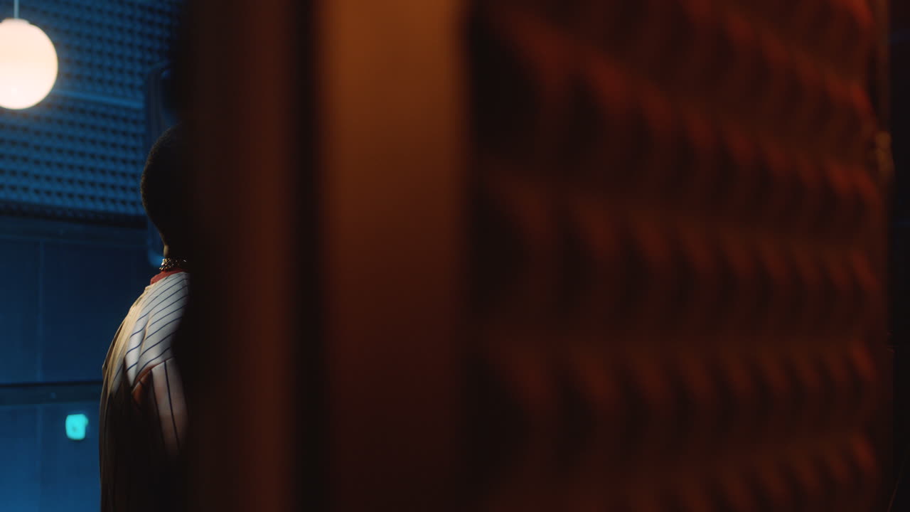 два молодых стильных парня-рэпера разговаривают и что-то решают, стоя в студии звукозаписи у микрофона и готовясь к записи песни