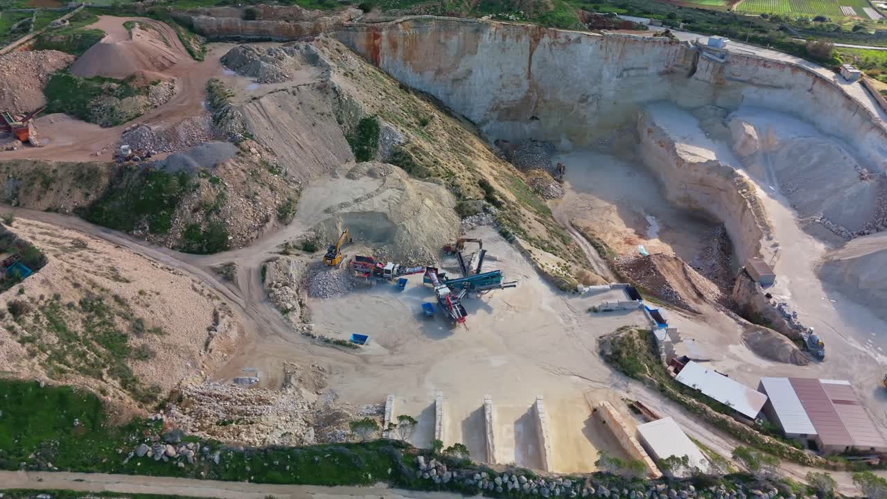 Aerial view of a limestone quarry in Mellieha, Malta, highlighting excavation machinery, storage areas, and surrounding greenery, showcasing industrial activity amid a Mediterranean landscape