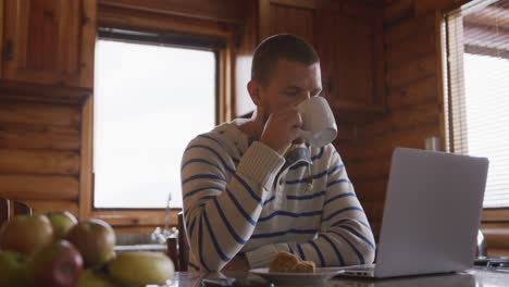 hombre caucásico pasando tiempo en casa, bebiendo una bebida, trabajando en una computadora portátil
