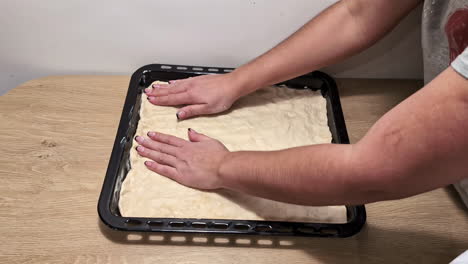 a time lapse of two people greasing a tin and placing dough and vegetables