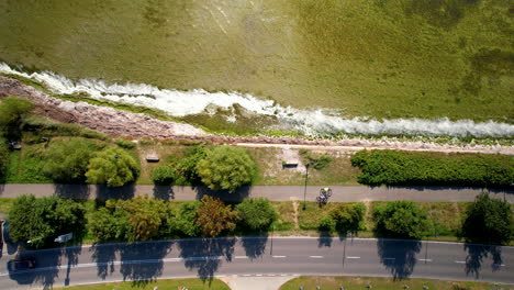 Cyclist-bikes-on-path-parallel-to-roadway-by-the-coast-as-ocean-waves-crash-on-rocks