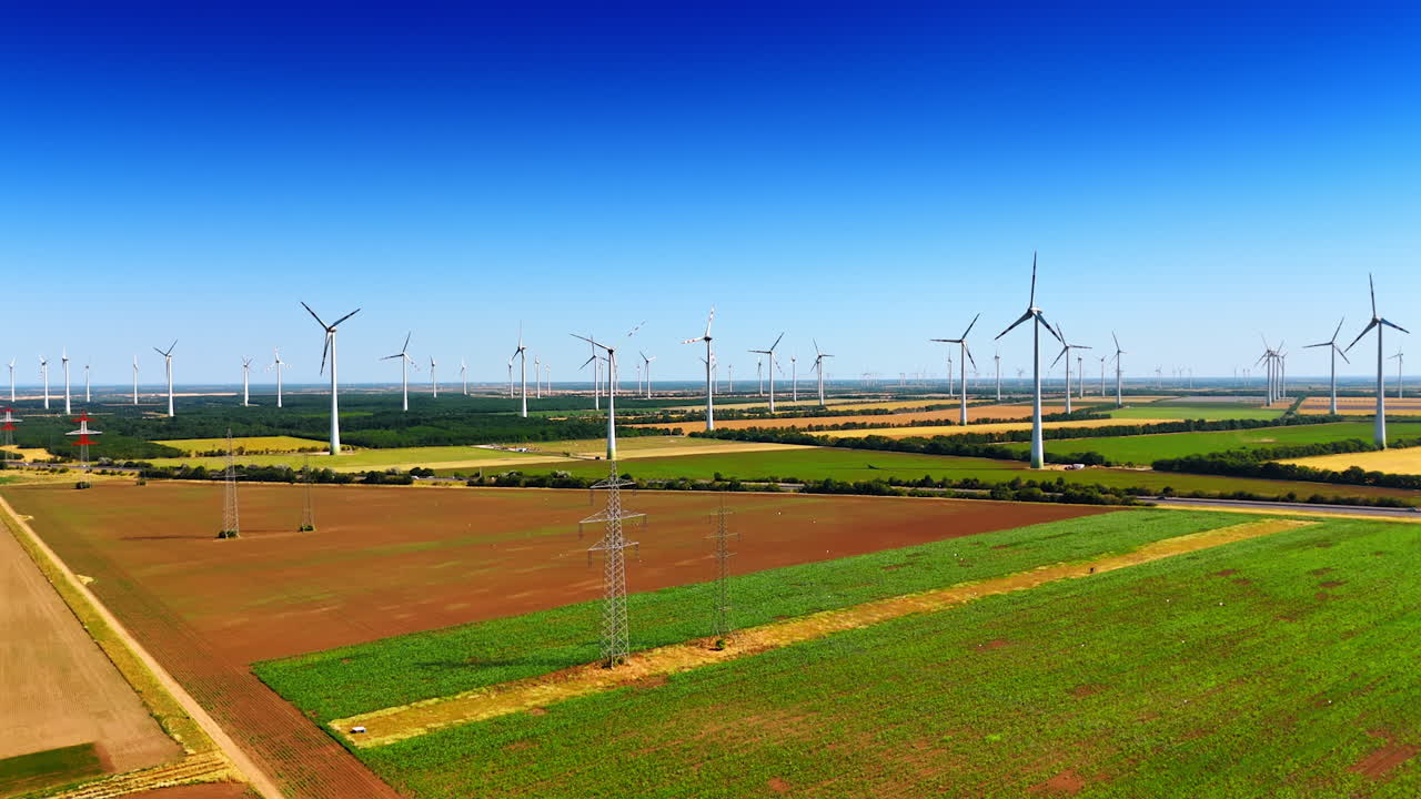 Numerous wind mills in the field produce green energy. Electric power lines along the highway in the countryside. Aerial view