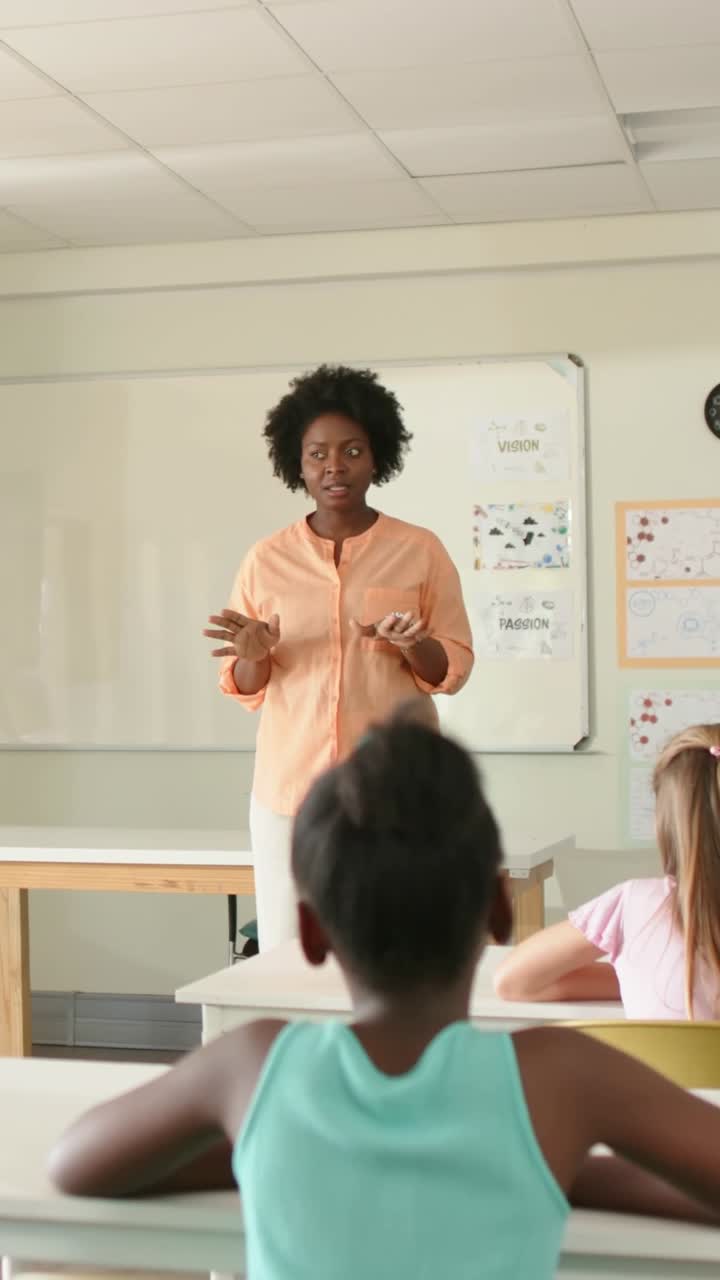 Starting female teacher in peach top gesturing while clarifying lesson at class front with board