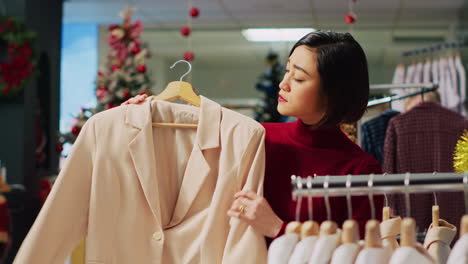 Porträt-Einer-Glücklichen-Frau,-Die-Während-Der-Winterferienzeit-In-Einem-Weihnachtlich-Geschmückten-Bekleidungsgeschäft-Durch-Elegante-Blazer-Auf-Regalen-Stöbert.-Lächelnder-Kunde,-Der-Modeboutique-Artikel-Prüft