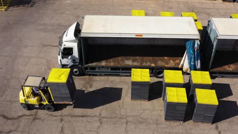Forklift-worker-loading-Medjool-dates-pallets-into-Shipping-trucks,-aerial-shot