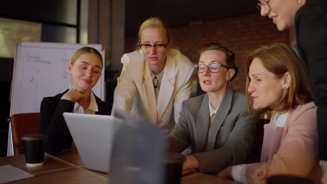 Middle aged girl speaker in glasses and gray uniform presenting her work during a meeting of businesswoman colleagues in a modern office