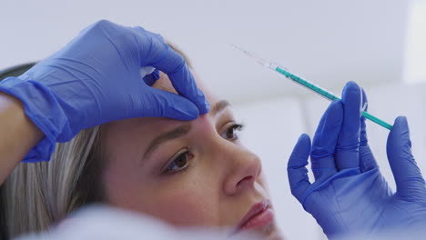 woman sitting in chair being give botox injection between eyes by female doctor