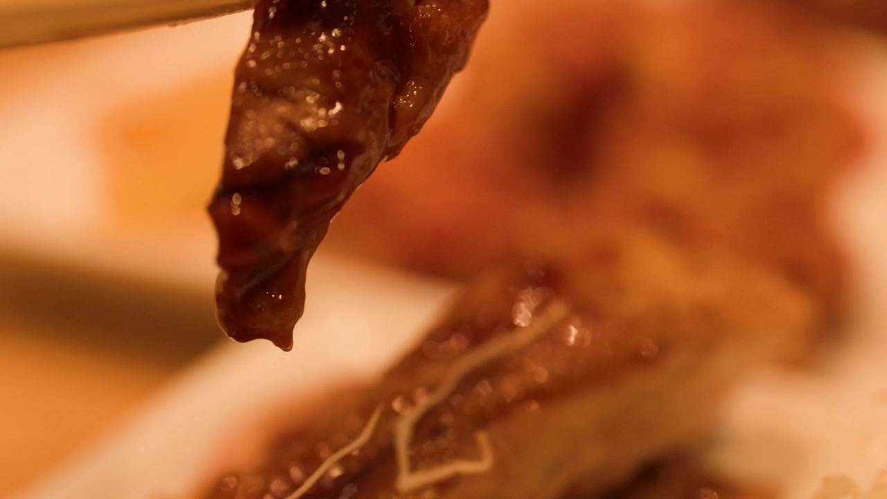 Close-up van eetstokjes die geglazuurde kip teriyaki van een bord pakken in Bangkok, Thailand